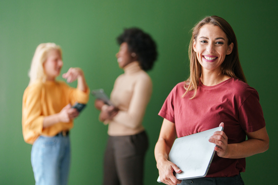 Femme au premier plan tenant une tablette, en arrière-plan deux femmes discutent